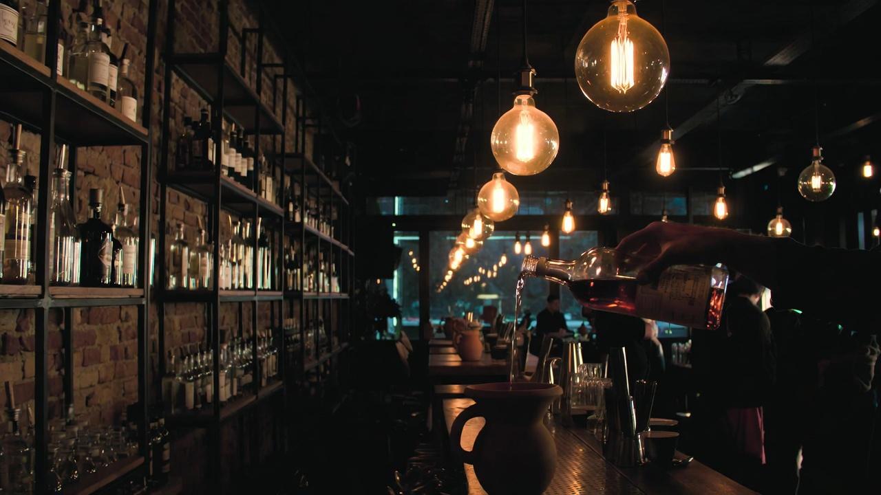 Dimly lit bar interior with shelves of bottles and warm neon lighting